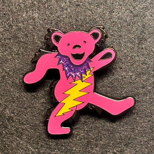 Pink cartoon-style bear with a purple heart and yellow lightning bolt on a gray surface