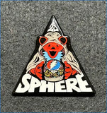 Triangular enamel pin featuring a smiling red bear in a white hooded robe holding a patterned sphere, with the word ’sphere’ below it.
