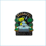 A yellow enamel grateful dead bear pin with white greenhouse and palm trees from dead and co golden gate park sf