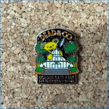 A Dead & Co Golden Gate Park enamel pin featuring the Grateful Dead bear, a white building, and green palm trees, displayed on a cork background.