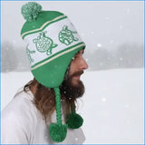 Green and white knit beanie with embroidered turtle patterns, ear flaps, and matching pom-poms on top and ends of the tassels.