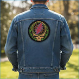 Blue denim jacket featuring a circular embroidered patch with a skull design, vibrant pink and green colors, and intricate detailing.