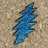 Blue glittery lightning bolt pin with a black outline.