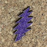 Purple glitter lightning bolt pin with a black outline.