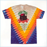 A vintage band t-shirt featuring a multicolor spiral tie-dye pattern in orange, yellow, blue, and purple. The front of the shirt displays a graphic of a black skull with a red glowing eye and the text 'MAD TOUR' in green, along with a printed concert tour schedule.