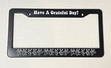 Black license plate frame with ’Have A Grateful Day!’ text and dancing skeleton figures.