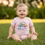 Baby sitting on grass wearing a pink onesie with a rainbow design.