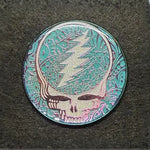 Metallic pin or badge featuring the Grateful Dead ’Steal Your Face’ skull logo in turquoise and silver tones.