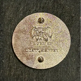 Metallic circular tag or medallion with an engraved design and two holes.