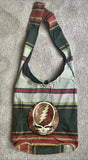 A striped, fabric shoulder bag featuring a prominent circular grateful dead skull logo in brown and white.
