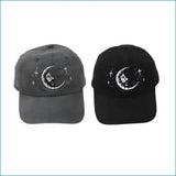 Two baseball caps, one in dark gray and the other black, both featuring a white embroidered design of a crescent moon with a face and small stars.